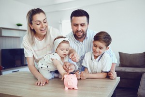 Family of four left to right consisting woman girl man and boy dropping coins in piggy bank