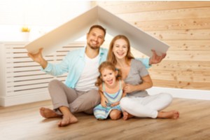 Family holding white cardboard making roof upon their heads while little girl sitting between them