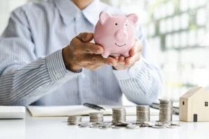 businessman holding piggy bank and raw coin with mini wood house